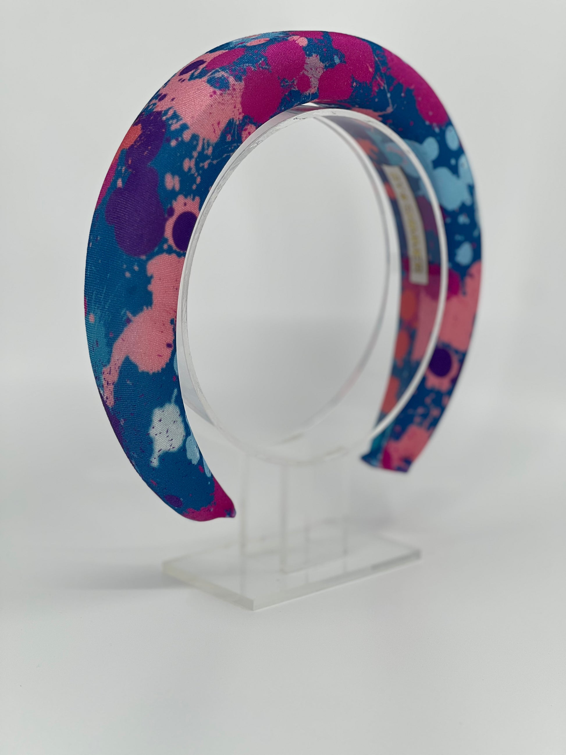 Colorful splatter-patterned headband on a clear stand against a white background